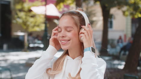 happy young woman taking off headphones after listening favorite energetic music on city street