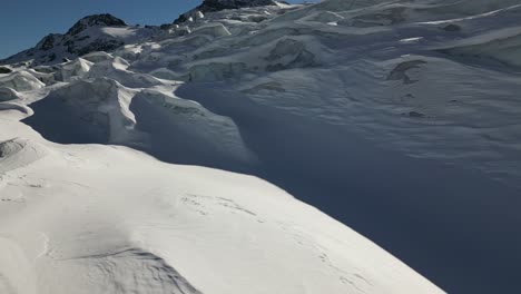 Aerial-push-in:-snow-covered-glacier-on-a-Swiss-alps-mountain,-icy-glacier-and-ridges