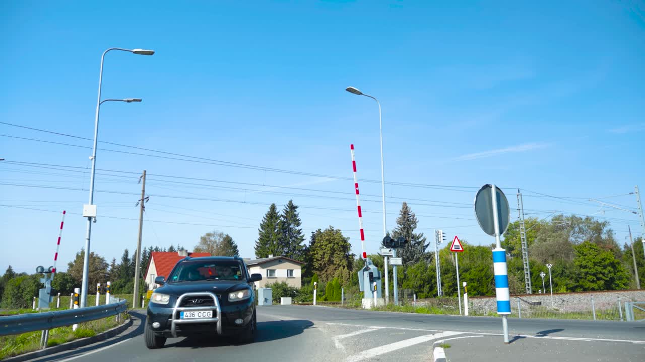 Timelapse or time lapse footage of Laagri Railroad crossing during summer time with blue sky while cars drive over the railway and wait in line when an electrical orange Elron train passes by.