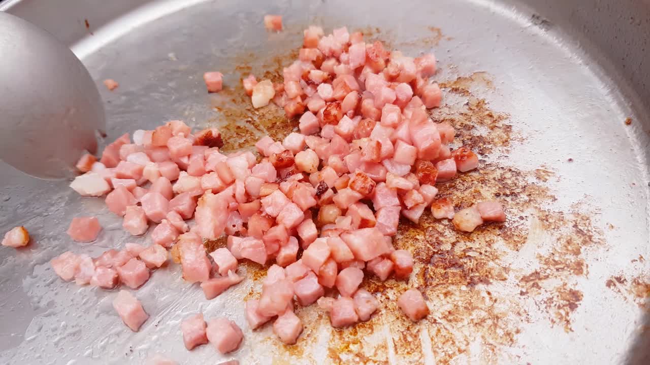 primer plano que se acerca a la sartén para acampar con cubos de tocino revueltos con una cuchara de metal