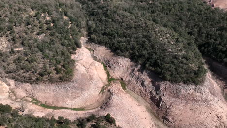 Rough-stone-woodland-topped-ravine-of-the-Sau-reservoir-during-drought-season-low-water-levels,-Catalonia,-Spain