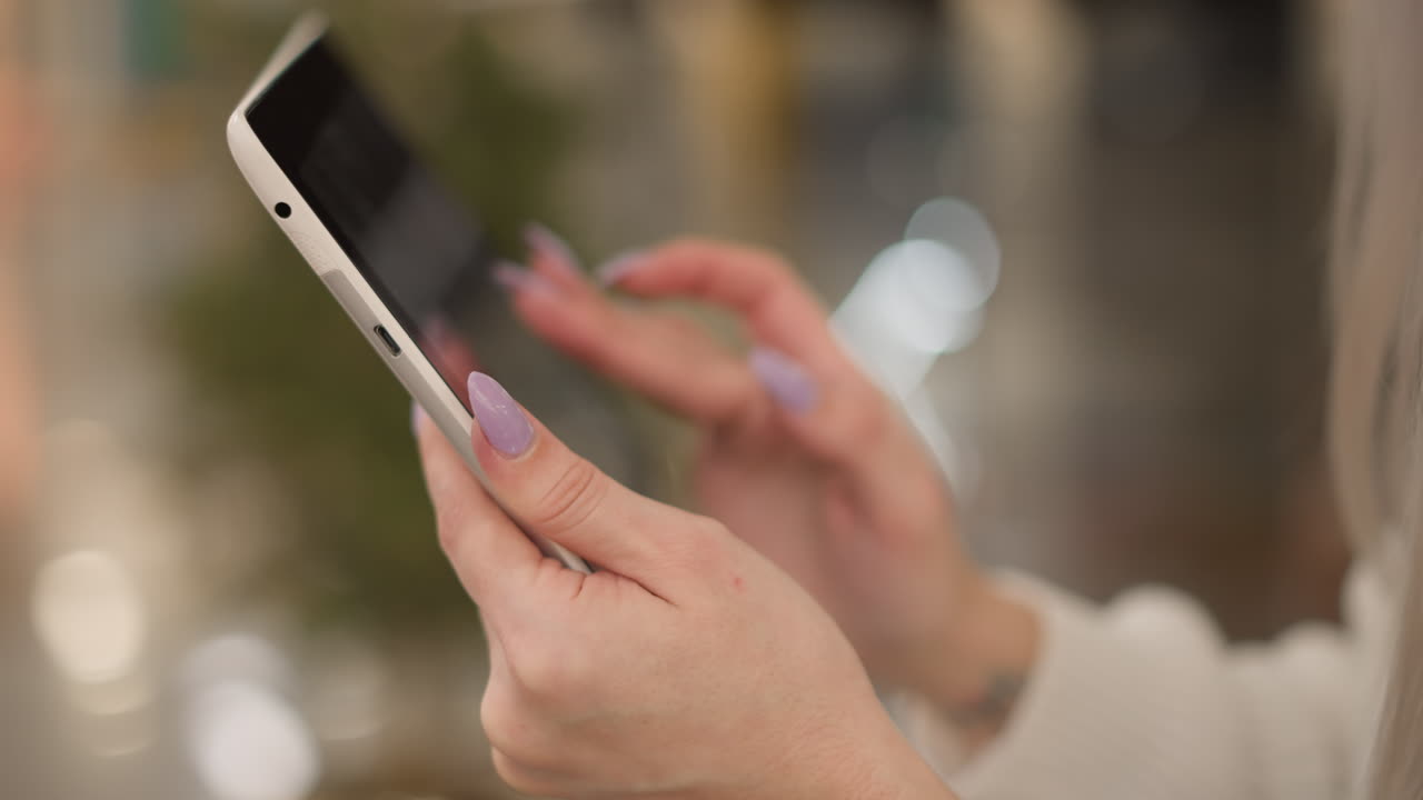 close up manicured fingernails tapping tablet screen held in hand against blurred mall interior with decorative bokeh lights capturing elegant digital interaction moment in modern retail seating area