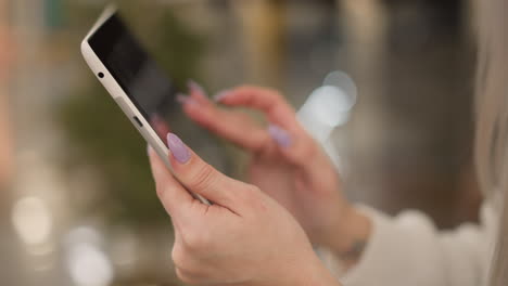 close up manicured fingernails tapping tablet screen held in hand against blurred mall interior with decorative bokeh lights capturing elegant digital interaction moment in modern retail seating area