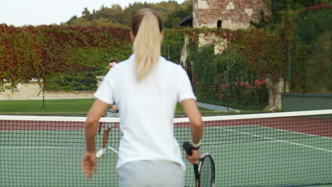 vista trasera de una mujer deportiva jugando tenis con un hombre en una cancha al aire libre en un día de verano