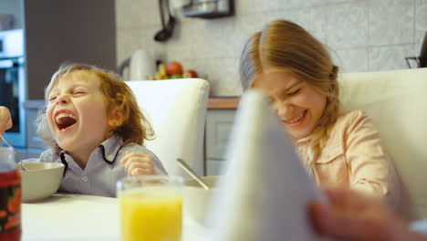 two siblings, a boy and a girl, having breakfast and laughing in the kitchen