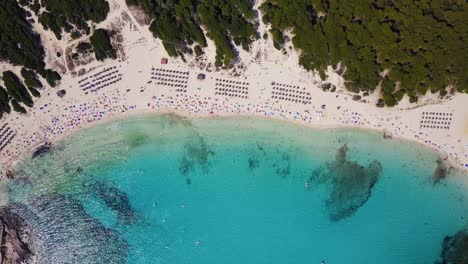 cala agulla, vibrant beach with tourists, clear turquoise water, and umbrellas, aerial view