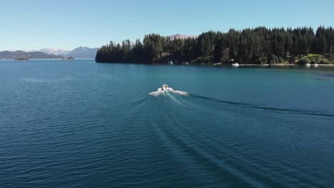 low aerial orbits small motorboat on clear deep blue lake in villa la angostura, patagonia