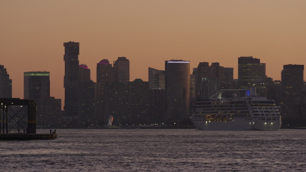 Crucero de pasajeros pasando por el perfil urbano de Nueva Jersey contra un cielo anaranjado al atardecer en el río Hudson