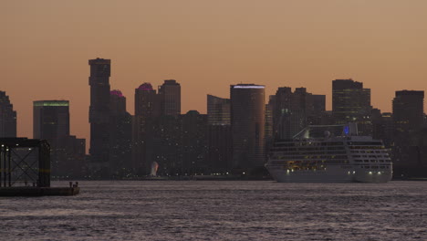 passenger cruise ship passing new jersey cityscape against orange sunset sky on the river hudson