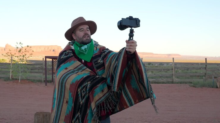 Man in Cowboy Hat and Poncho Vlogging in Desert Landscape