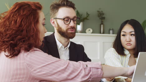 group of three multiethnic colleagues sitting at table and debating while looking at laptop computer