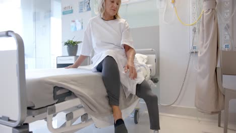 paciente mayor caucásica con pierna protésica sentada en la cama del hospital