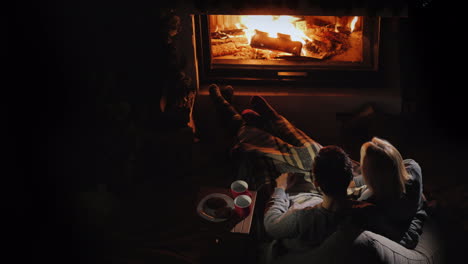 a young couple admires the fire in the fireplace sitting next to them and drinking tea romantic dinn