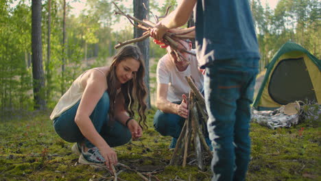 familias en la naturaleza juntas recogen e instalan un fuego para cocinar. viaje familiar al bosque. caminata con una tienda y una estancia nocturna en el bosque junto al fuego