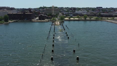 low flying drone shot over an old, partly sunken, abandoned pier, with the sun shinning - shimmering onto the waters below