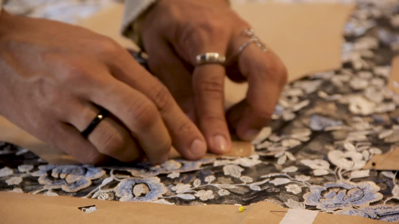 mani maschili nere che attaccano i perni al modello di cucito sulla parte superiore di un tessuto testurizzato floreale - interno primo piano palmare