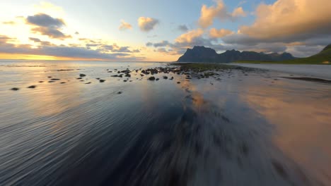 speeding drone flight over coastline of lofoten with rocks in flat water during golden sunset