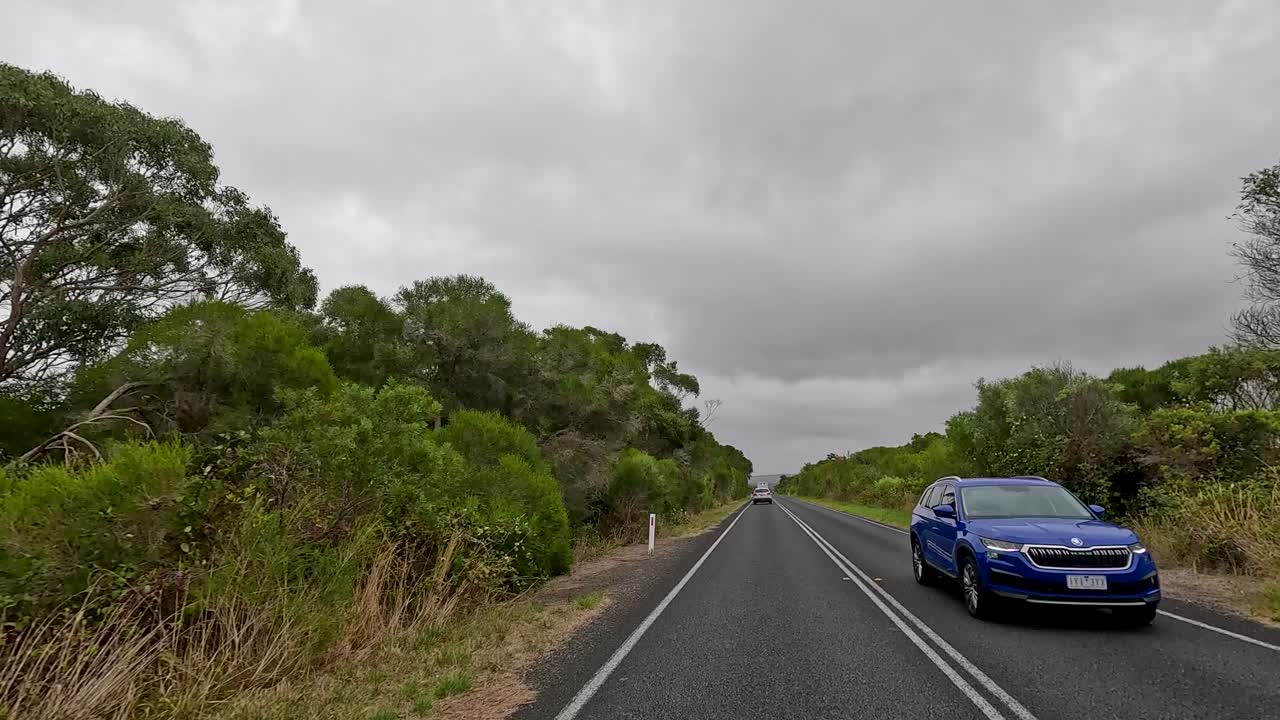 A fast-motion drive along a rural highway on the Great Ocean Road, Victoria, Australia, with lush greenery, cloudy skies, and smooth forward camera movement