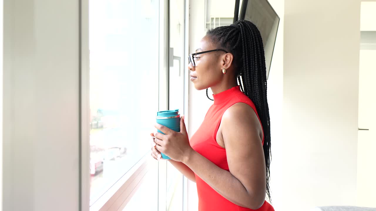 Woman in red dress looking out the window with a coffee cup