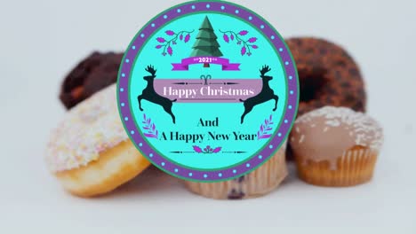 Animation-of-christmas-greetings-on-tag-over-cupcakes-on-white-background