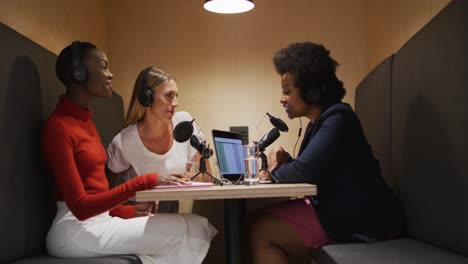 three diverse female radio hosts wearing headphones talking on microphone for radio podcast