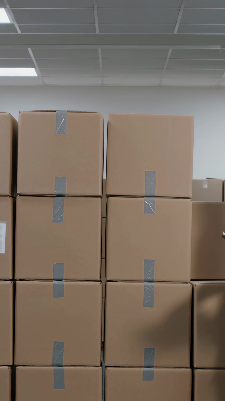 Vertical video: Entering right forearm gesturing at stacked cardboard boxes in stockroom, with tape