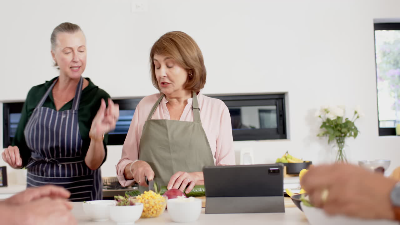 Cooking together, senior friends preparing meal with tablet in kitchen