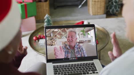 Diverse-senior-female-friends-using-laptop-for-christmas-video-call-with-happy-man-on-screen
