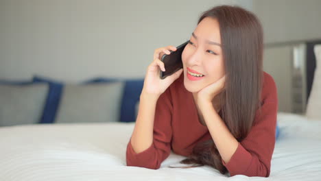 portrait of young asian woman making phone call with smartphone, lying on bed, close up