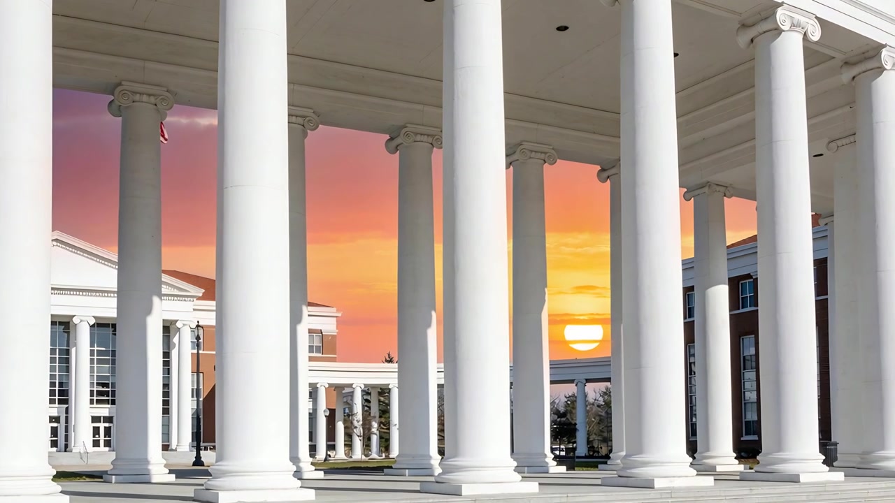 Sinking sun moving through rectangular opening, bathing white Ionic colonnade and paved plaza