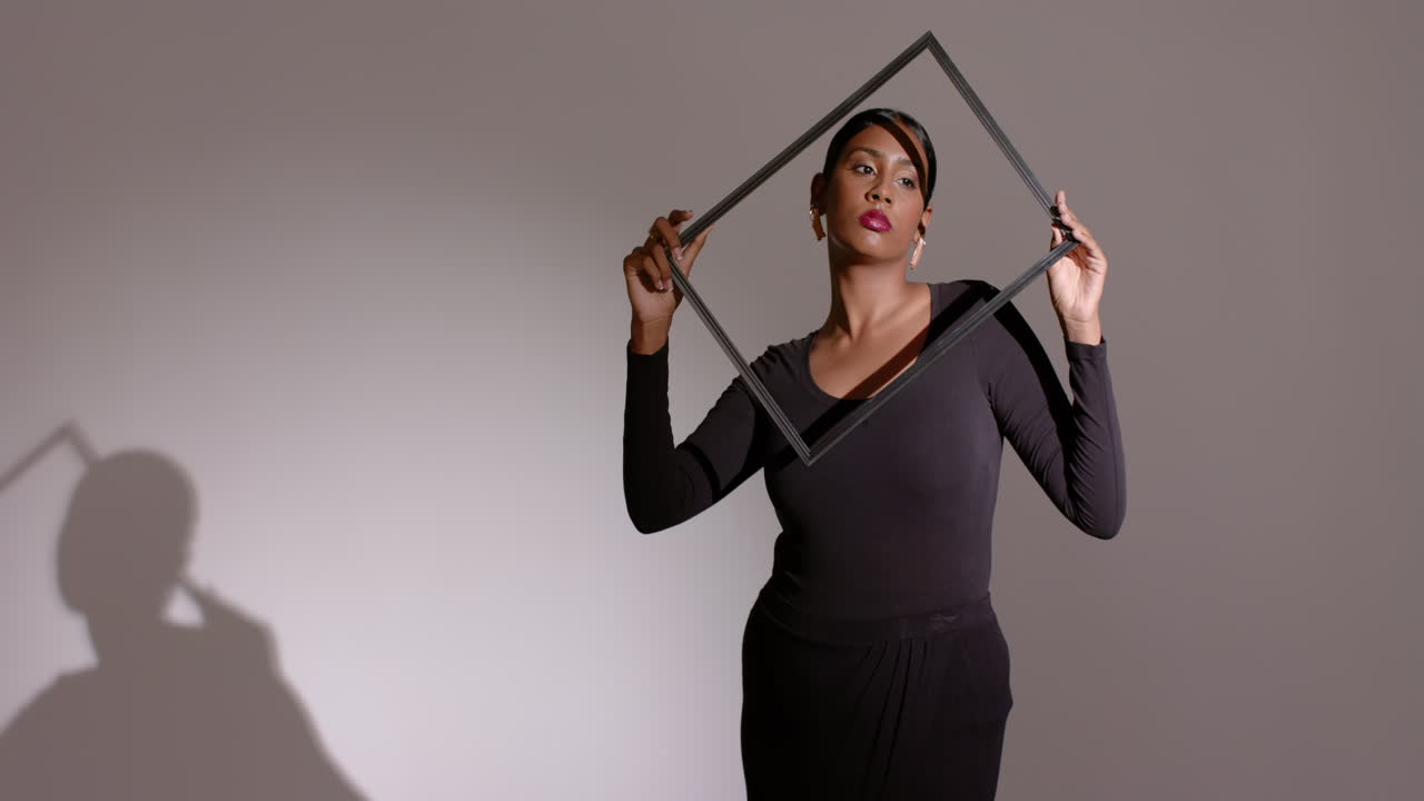 Under sidelight in studio, Indian woman model rotating black metal frame creating dramatic shadows