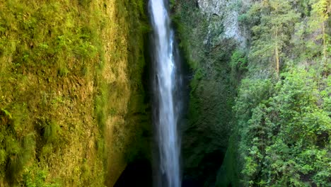 dolly out of hidden mili mili misty waterfall falling into natural pool surrounded by dense green vegetation, coñaripe, chile