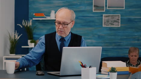 un hombre de negocios senior leyendo informes sentado frente a una computadora portátil.