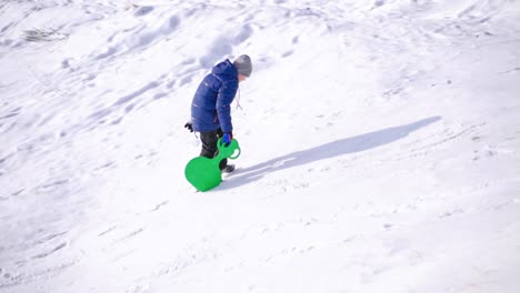 child boy having fun on snowy winter walk in nature. frost winter season.cute little boy with saucer sleds. winter games and fun.