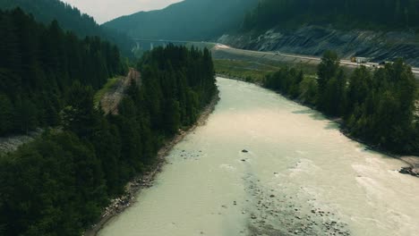 cinematic aerial tilt-up, moving down and forward opening shot of the kicking horse river in british columbia, canada, partly hazy due to wildfires at time of recording, drone