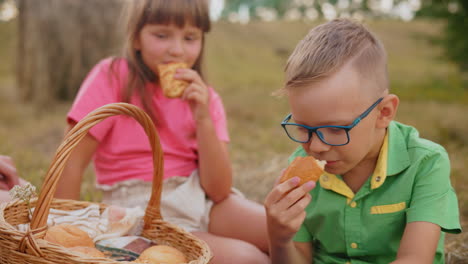 dos hermanos sentados en un campo abierto disfrutando de pasteles recién horneados, sonriendo y compartiendo un momento de alegría mientras disfrutan de la belleza de la naturaleza a su alrededor en un entorno rural pacífico
