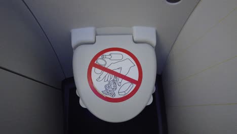 airplane onboard bathroom toilet seat with lid closed and prohibited objects warning sign on it