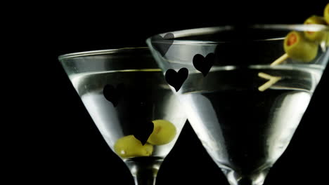 animation of hearts floating over glasses of martini on black background