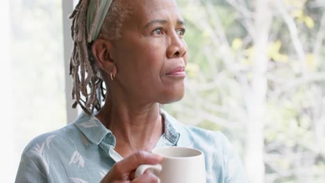 Nachdenkliche-ältere-Afroamerikanische-Frau,-Die-Kaffee-Trinkt-Und-Zu-Hause-Aus-Dem-Fenster-Schaut,-Zeitlupe