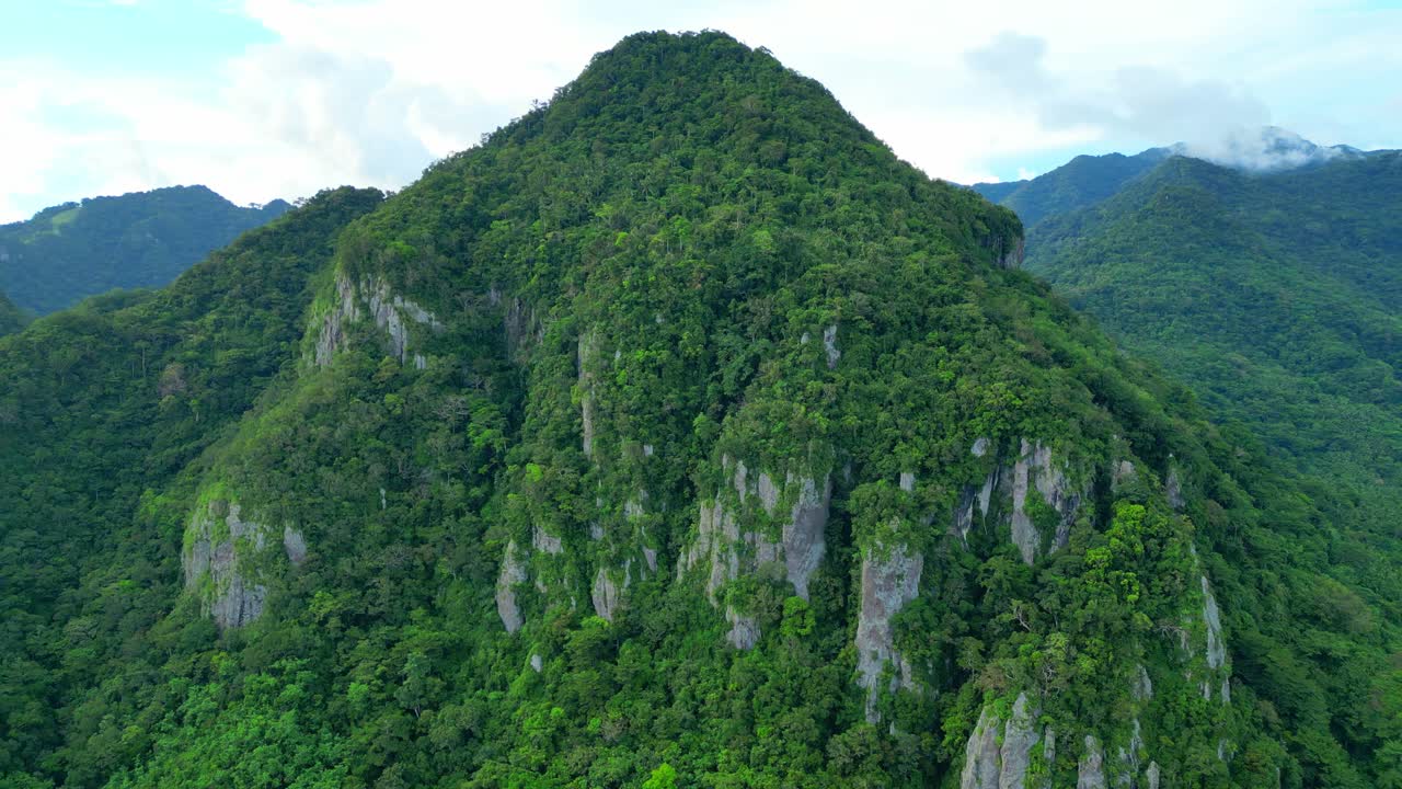 Bidikan aerial pan kiri dari tebing batu kapur yang menonjol yang dikenal sebagai Tulay na Busog di Lobo, Batangas, yang ditutupi hutan tropis lebat dan bebatuan bergerigi