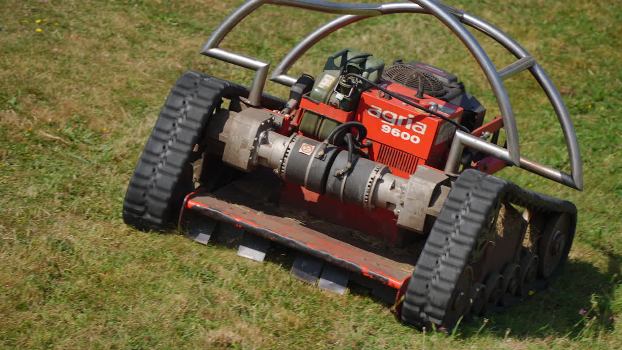 GIJON, SPAIN - AUGUST 3, 2025: Detail view of the Agria 9600 robotic slope mower cutting grass on a steep terrain. The tracked equipment is part of urban landscaping services in the city of Gijon