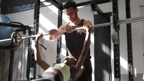 woman bench pressing with trainer in gym