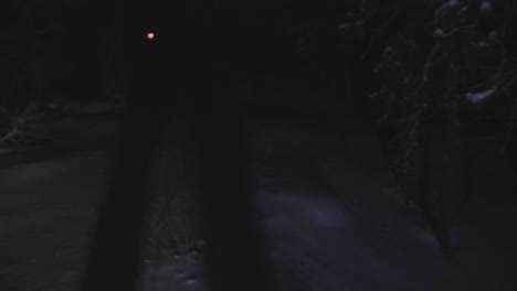 person walking on snow in complete dark with flashlight, reaching the moon