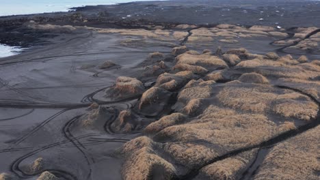 sandvik playa de arena volcánica negra con huellas de neumáticos de motocross y dunas cubiertas de hierba, antena