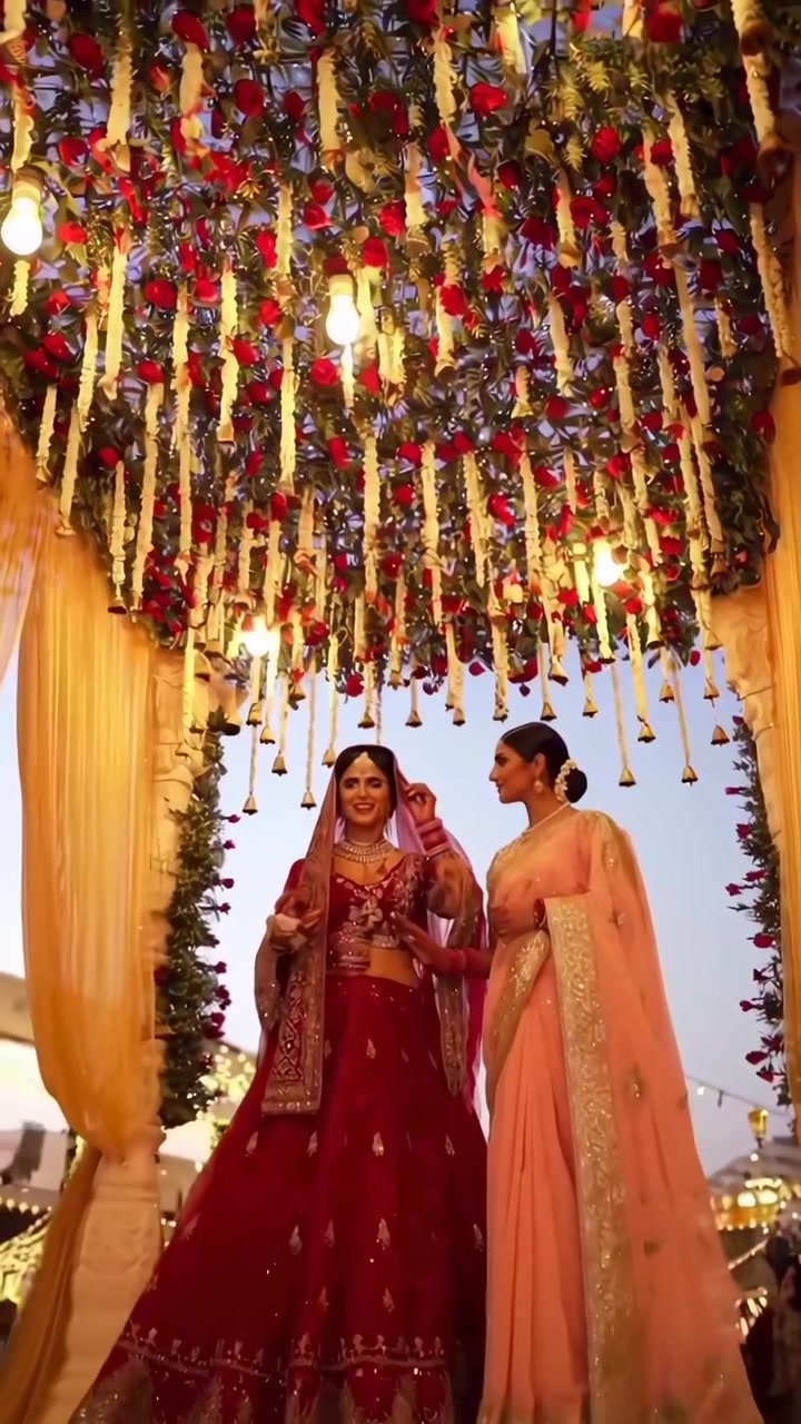Indian Bride and Bridesmaid Standing Under Floral Wedding Canopy