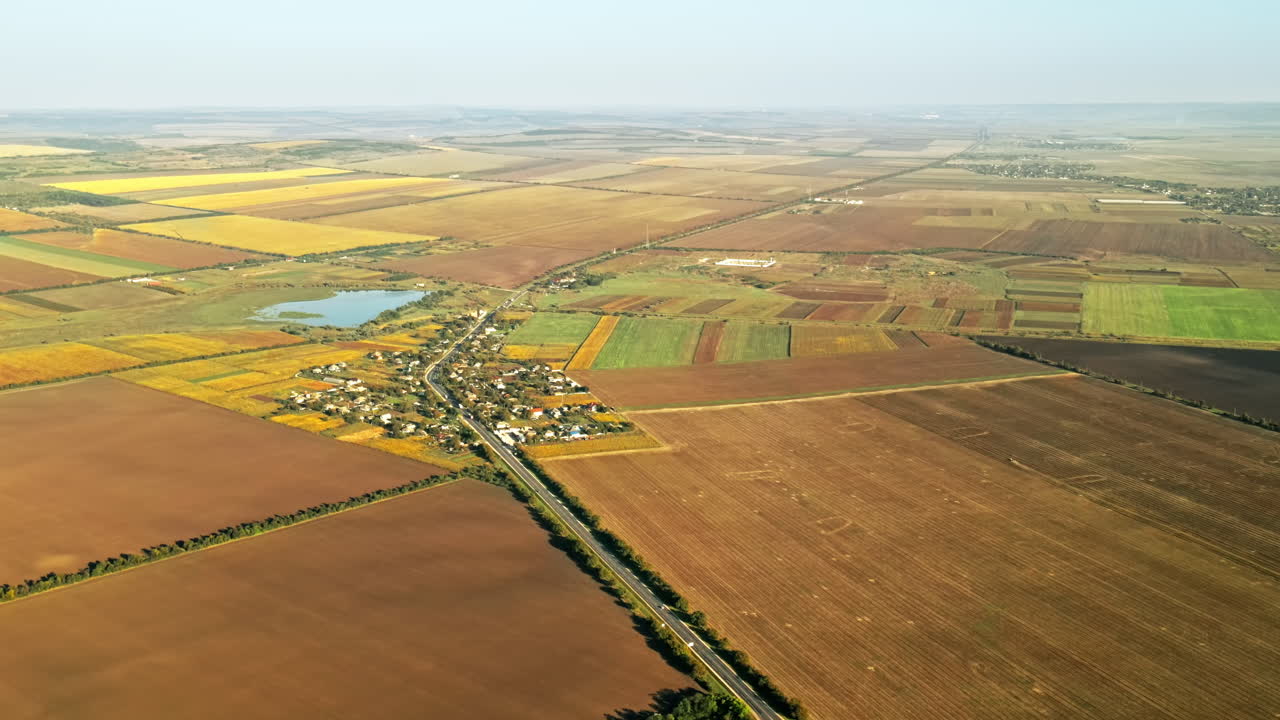 Aerial drone view of village in Moldova. Residential buildings, road with moving cars, lake, fields around