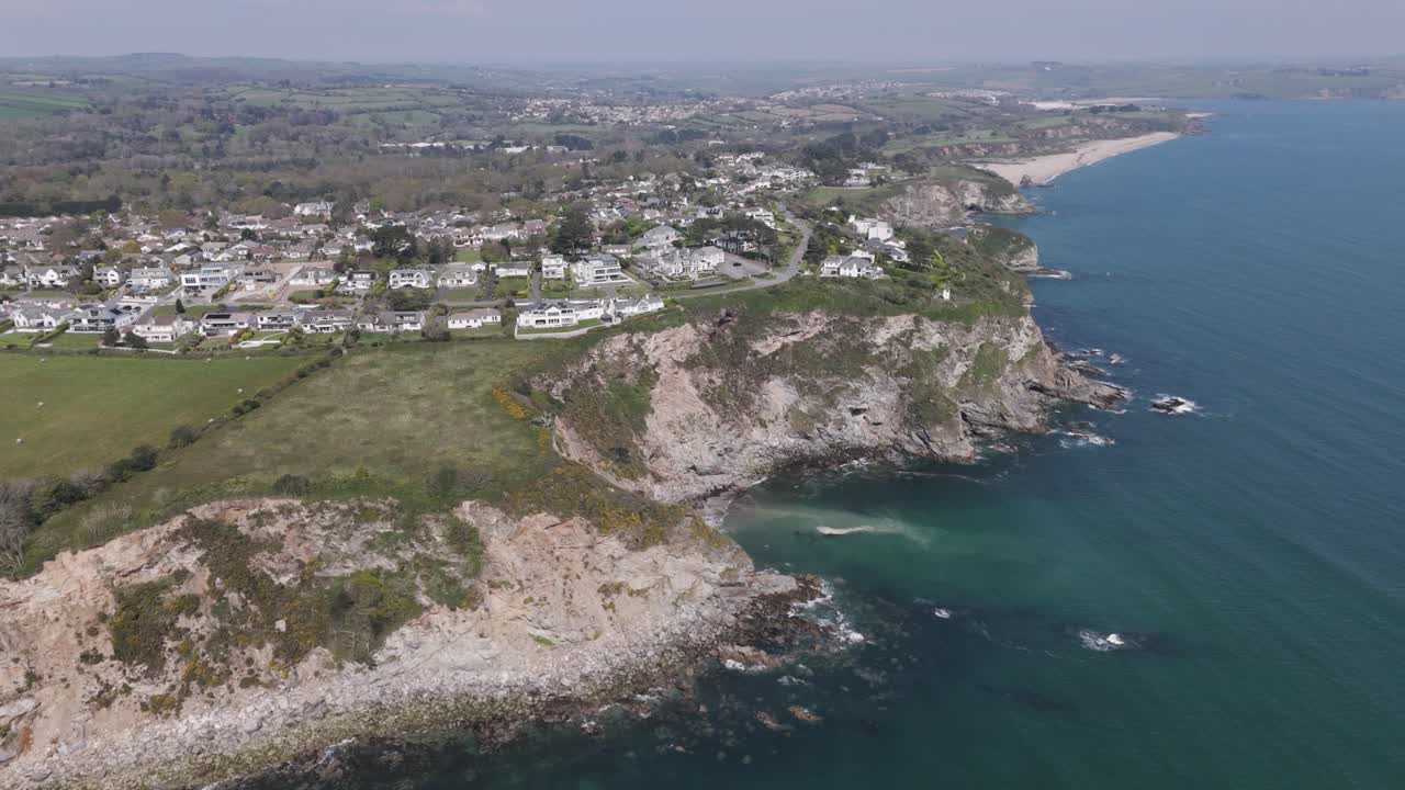 Aerial sweep across rugged headland where upscale homes perch above deep blue coves and inlets, grassy cliffs meeting the ocean to showcase premium seaside real estate