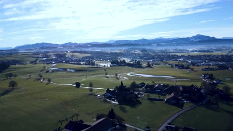 Alps-in-the-distance,-looking-onto-a-green-Landscape-from-the-top-with-a-drone,-bird-view