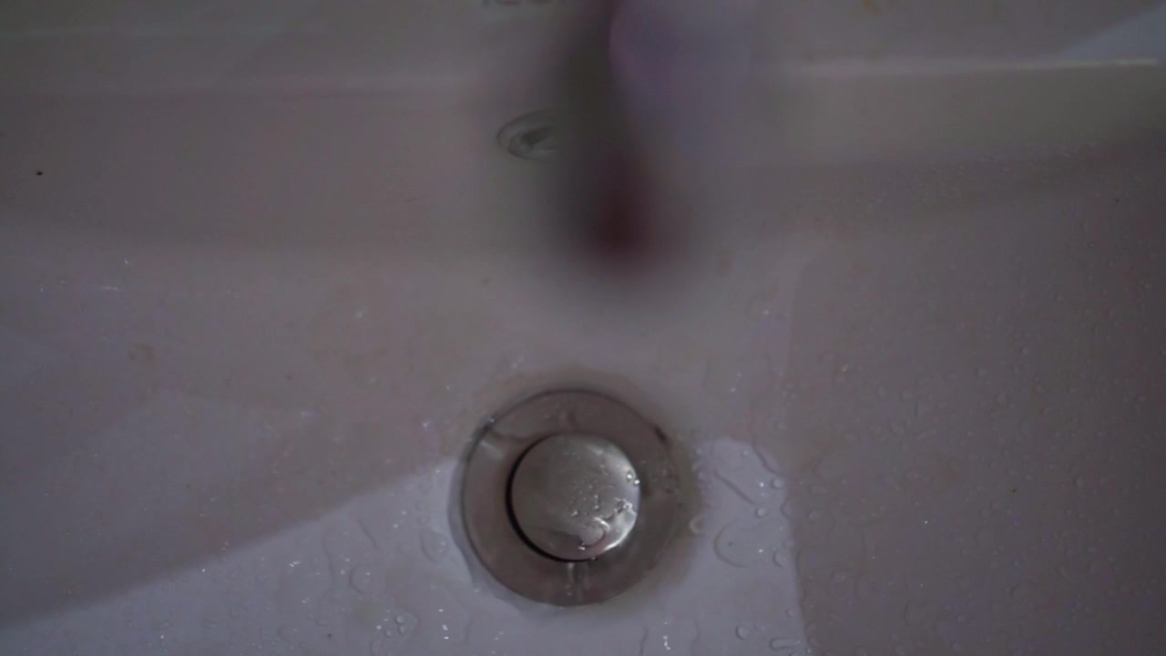 Water drops on metal sink drain plug, close up shot, bathroom or kitchen plumbing, wet ceramic surface, cleaning concept scene.