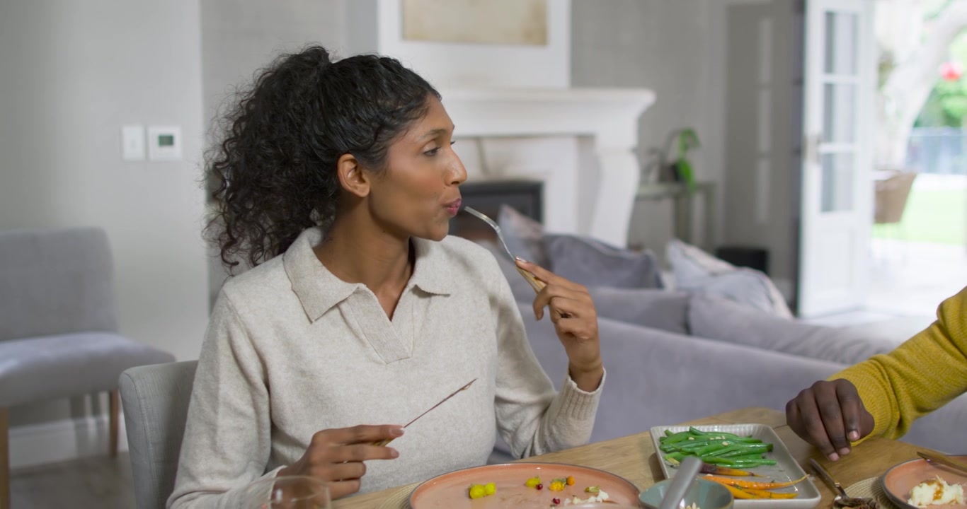 African American couple, woman cutting salad with fork tasting reacting to partner speaking at home